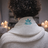 Coussin cervical chauffant en coton nid d'abeillel porté sur les épaules, conçu pour soulager les tensions et favoriser une relaxation profonde, ambiance spa avec bougies