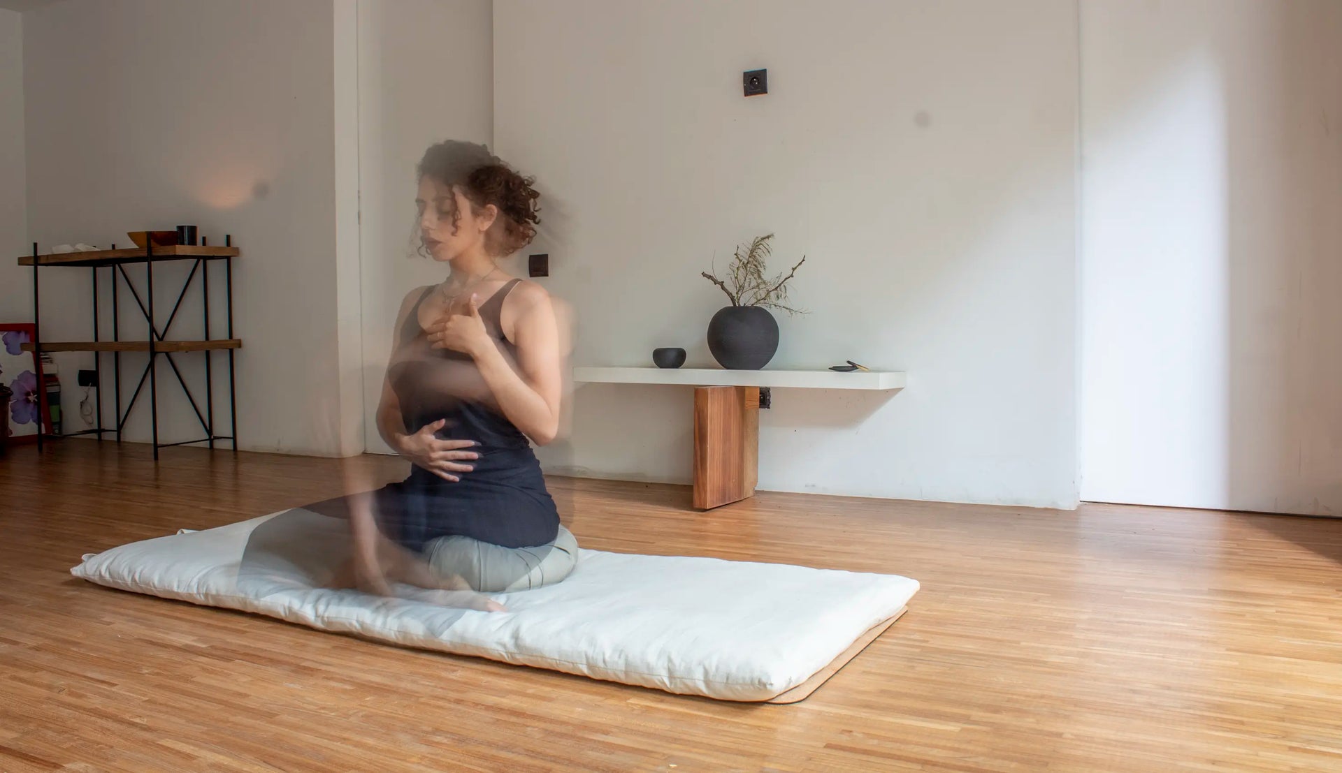 Femme assise en posture de respiration consciente sur un futon artisanal en lin naturel, dans un espace de méditation lumineux fabriqué au Maroc.