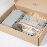 Coffret de relaxation en carton kraft contenant un tour de cou en lin rempli de lavande et graines de lin, un masque pour les yeux à la lavande, un bâton de sélénite, un bâton de palo santo, un fagot de sauge blanche et de la paille décorative.