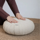 main posée délicatement sur la texture d'un coussin de méditation à plis zafu en lin naturel beige