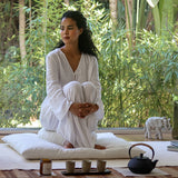 Femme assise en tailleur sur une ensemble de coussins de méditation dans son coin zen à la maison