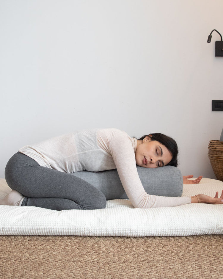 femme assise en posture restorative de yoga sur futon et bolster de yoga
