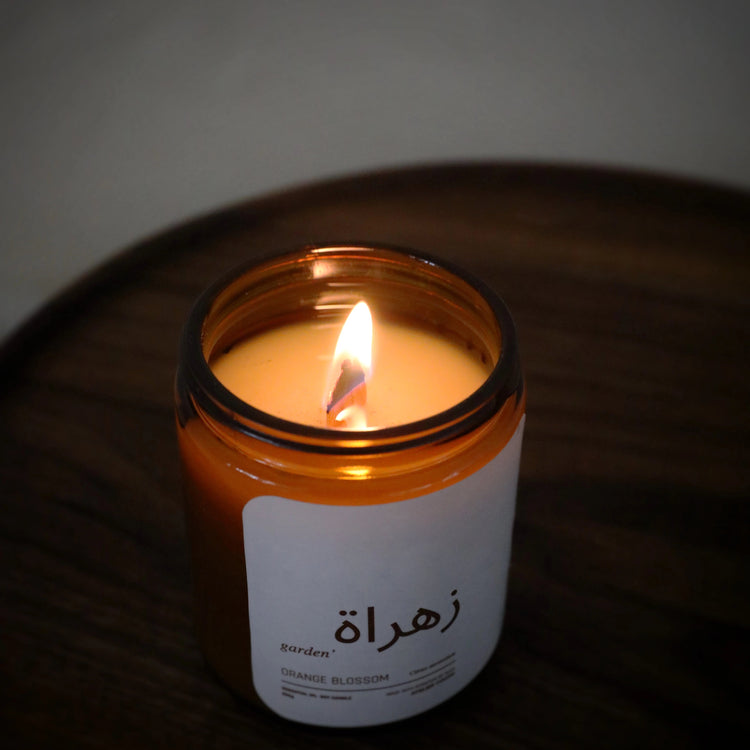 Bougie artisanale en cire de soja avec mèche en bois allumée, pot ambré sur plateau en bois.